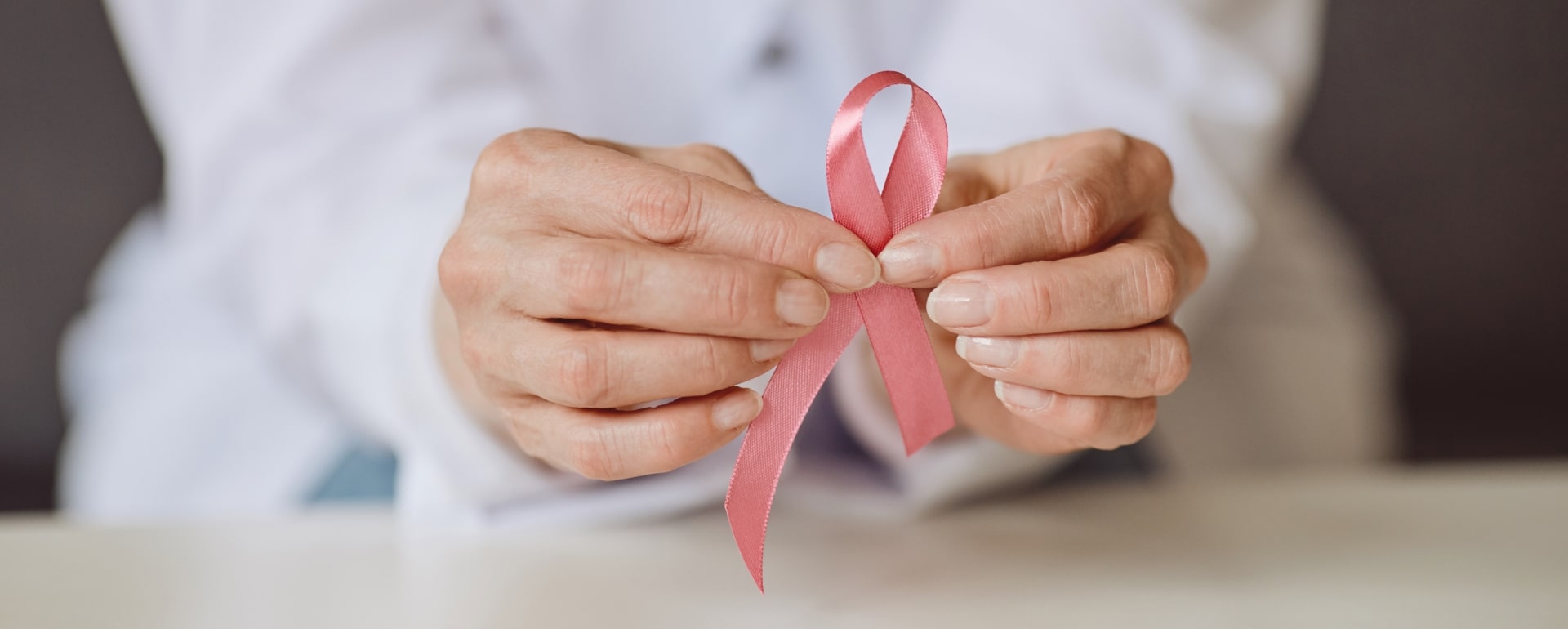 różowa wstążka, symbolem raka piersi trzymana w palcach dłoni